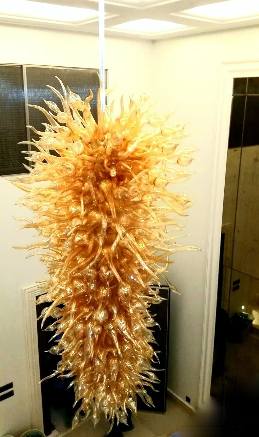 Large golden amber glass petal cascade chandelier hanging in a pale interior