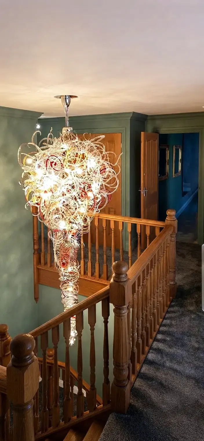 Sculptural glass wire chandelier with white and red swirls above a traditional wooden staircase
