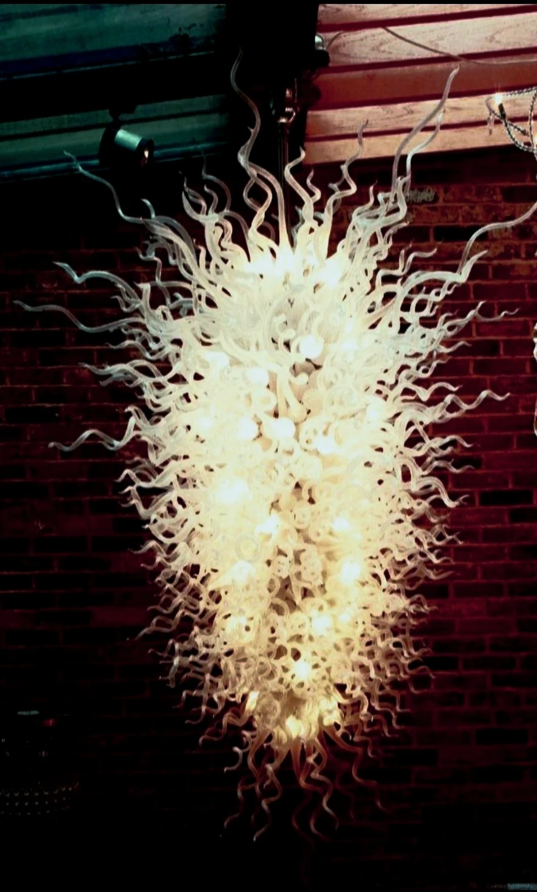 Sculptural white glass tendril chandelier against an exposed brick wall
