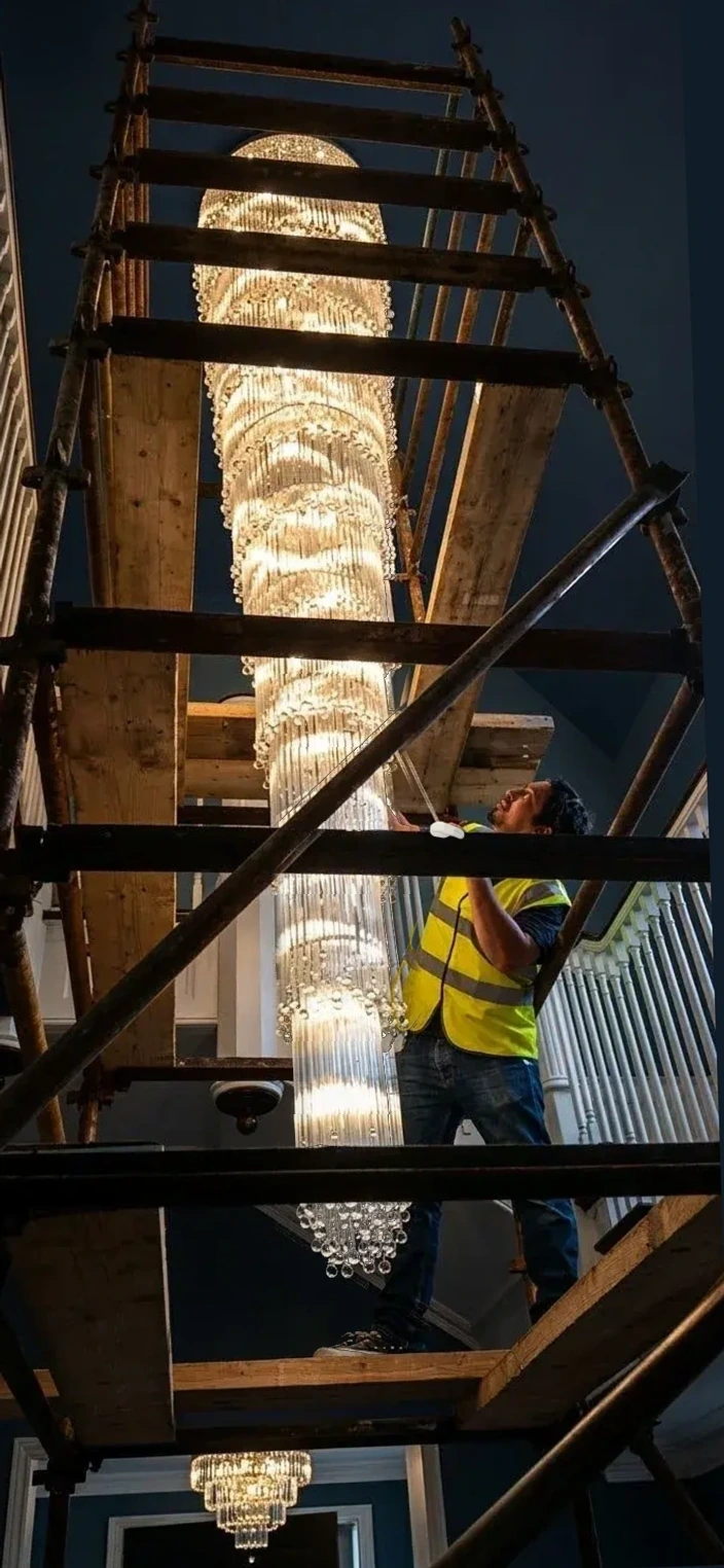 Chandelier specialist in a high-visibility vest cleaning a tall cascade chandelier from scaffolding