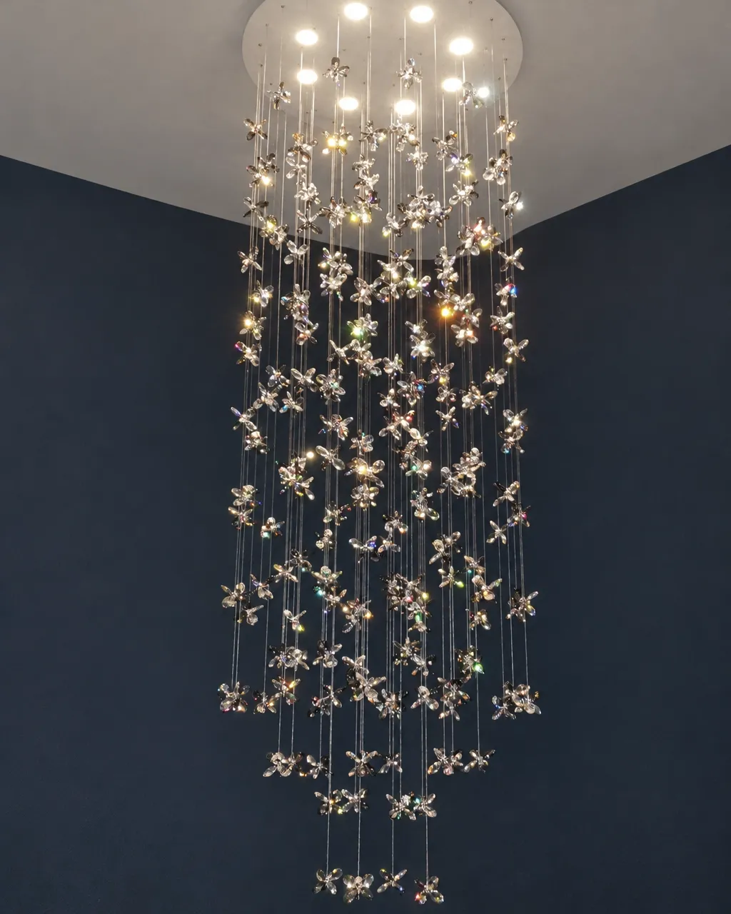 Illuminated cascade chandelier with delicate crystal flower details against a dark wall