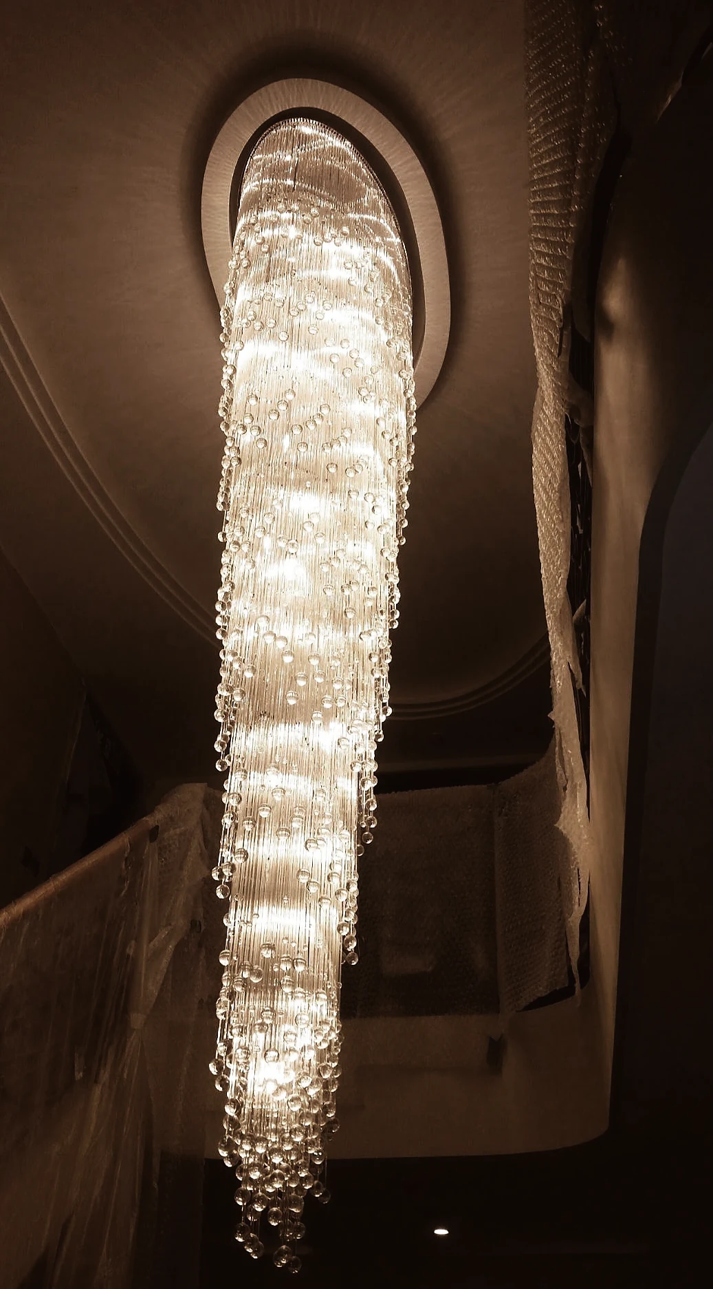 Crystal rod cascade chandelier hanging from a circular ceiling rose in a bright stairwell