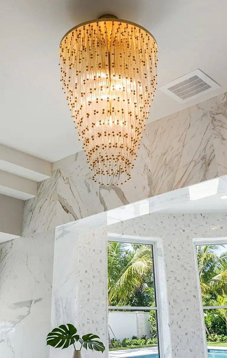 Gold beaded cascade chandelier in a luxury marble interior overlooking a pool