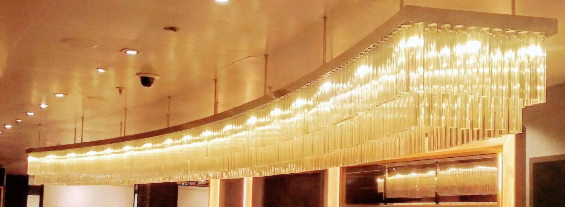 Long illuminated gold crystal chandelier spanning a luxurious interior