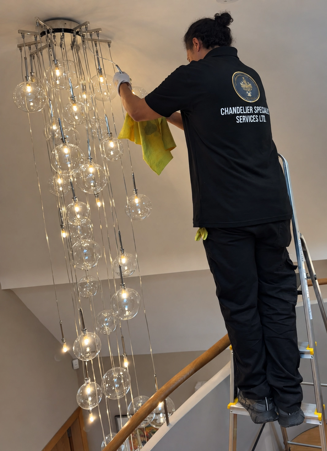 Specialist working from a ladder beneath globe pendant lights