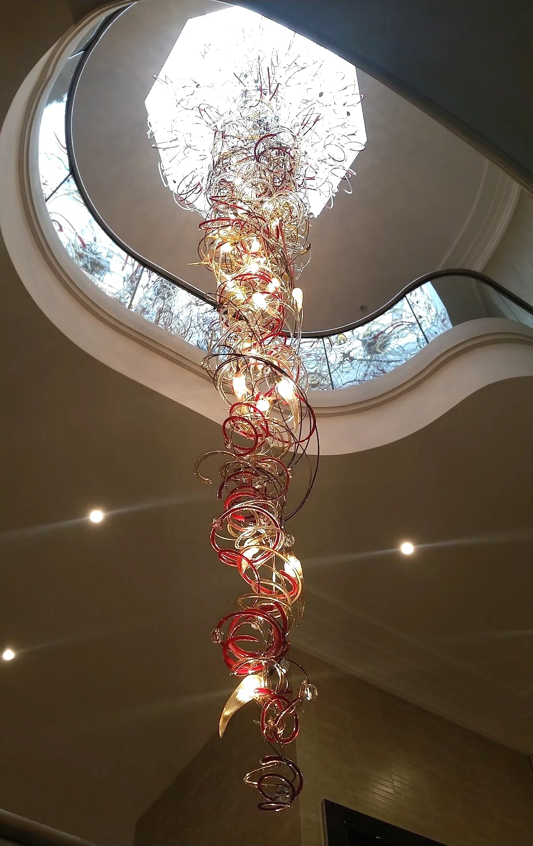 Red and gold glass wire cascade chandelier seen from below beneath a skylight