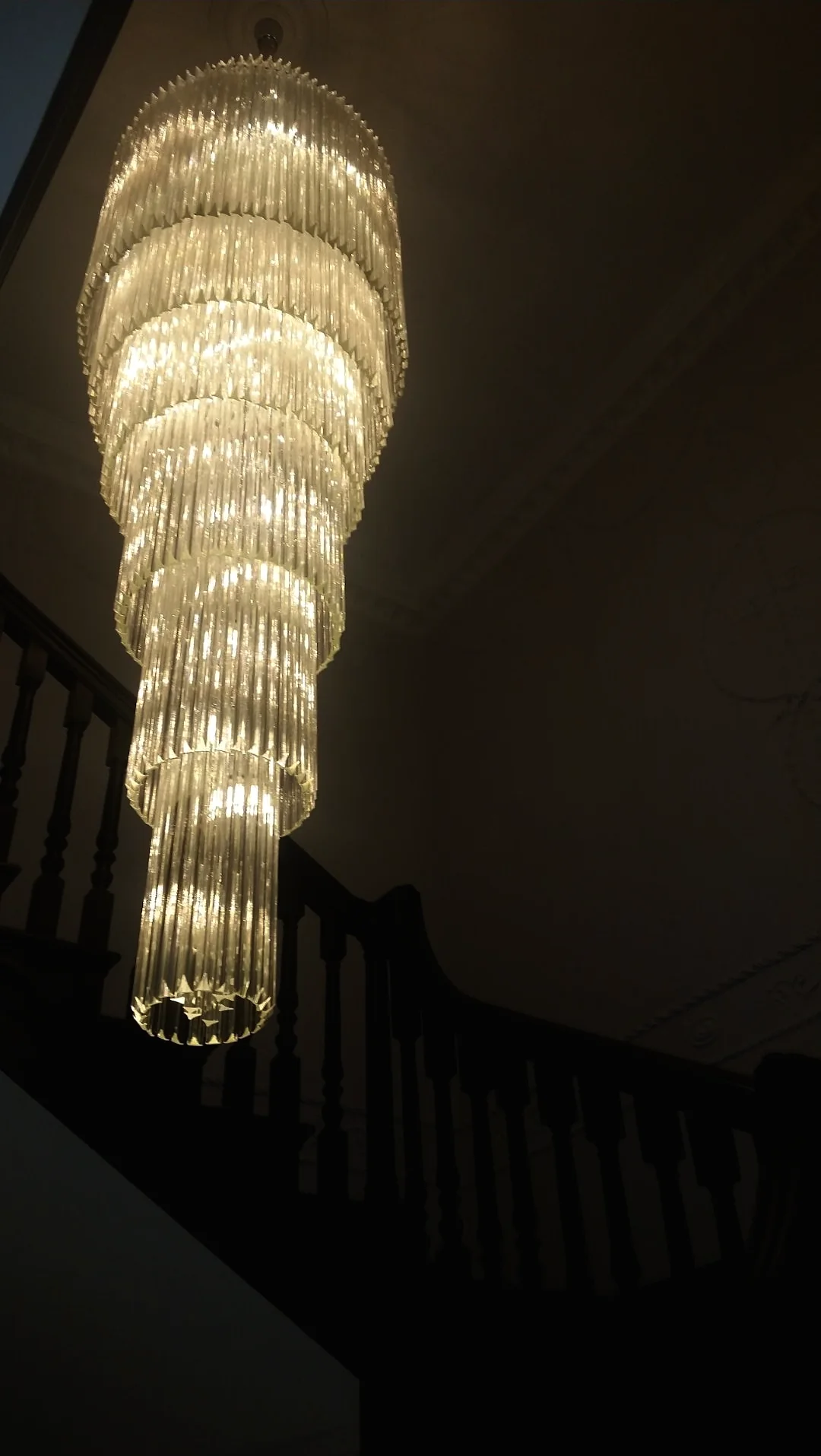 Tiered crystal tube cascade chandelier glowing in a dark stairwell
